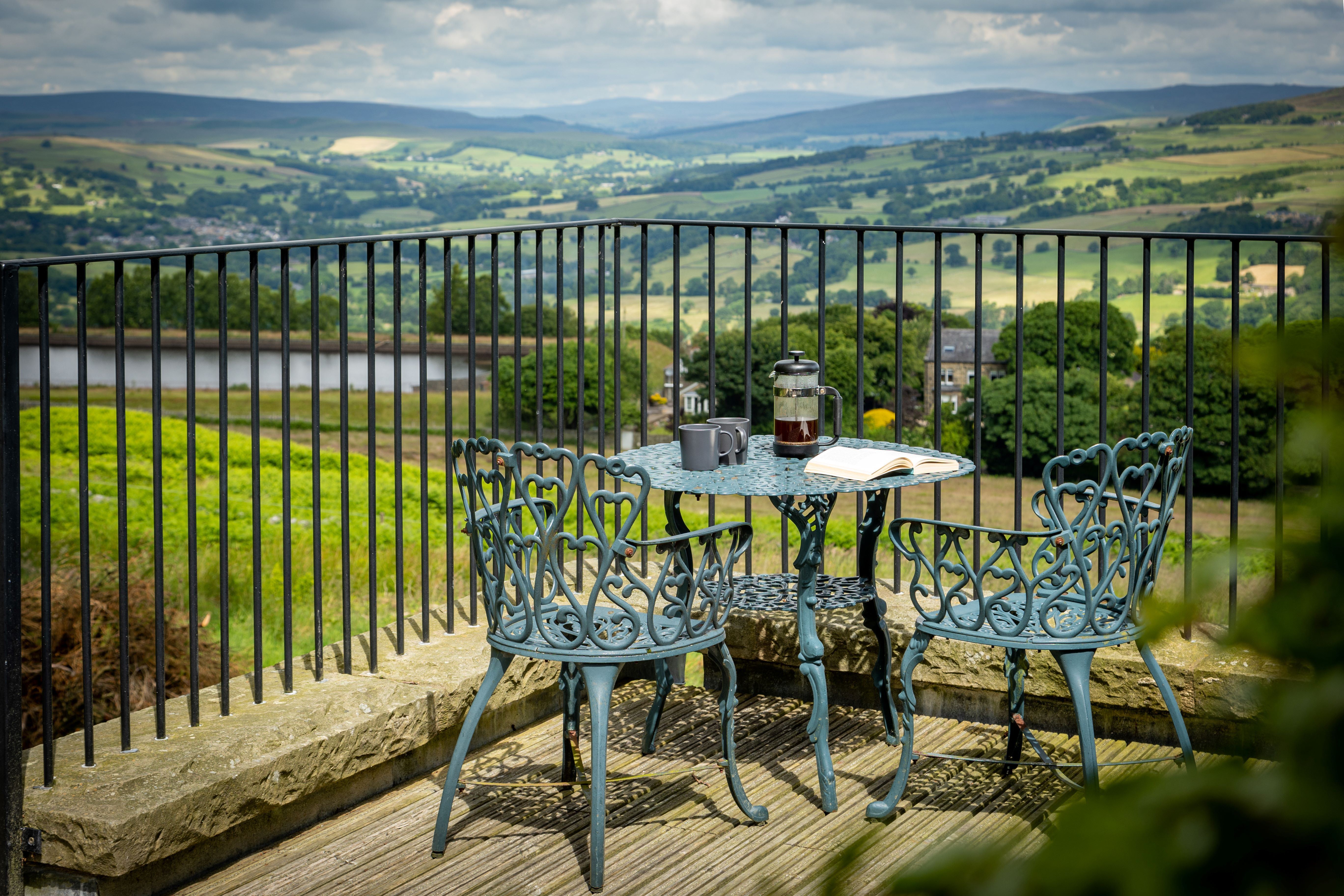 Black cast iron patio table with two chairs on a raised terrace with a view of rolling hills in the background