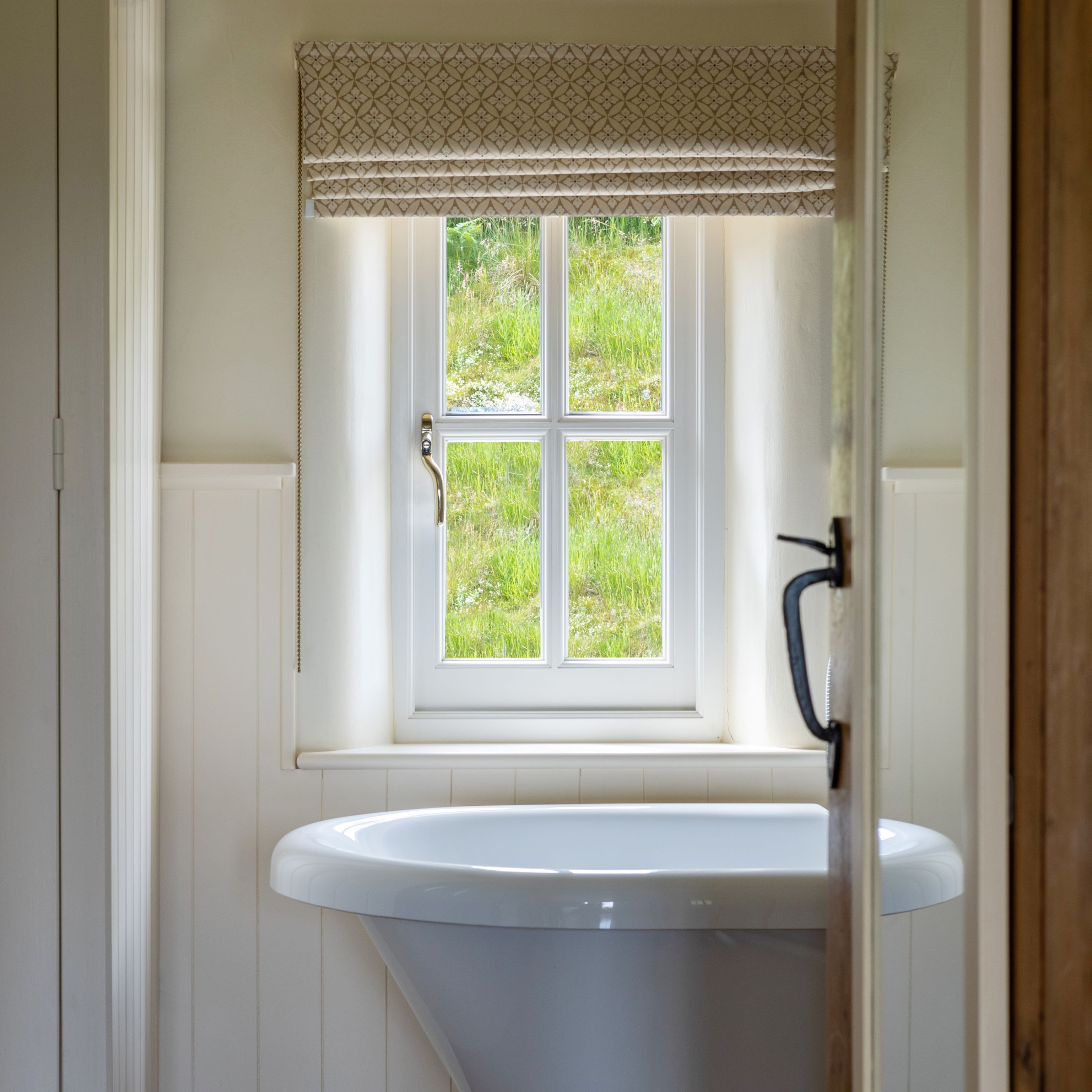 White roll top bath below a small window