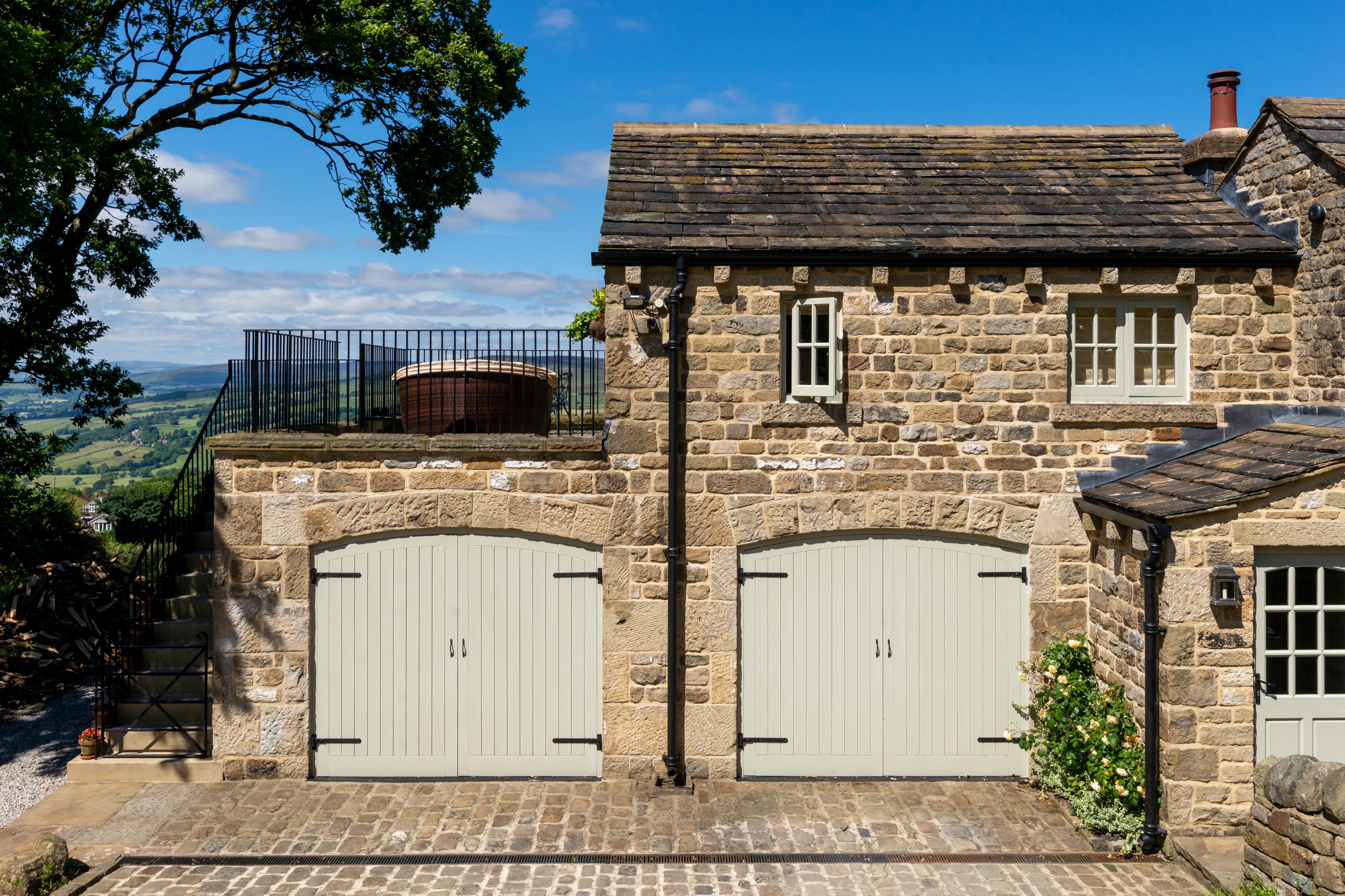 A two storey Yorkshire stone building with wooden garage doors on the ground floor and stone steps up the side to a first floor terrace