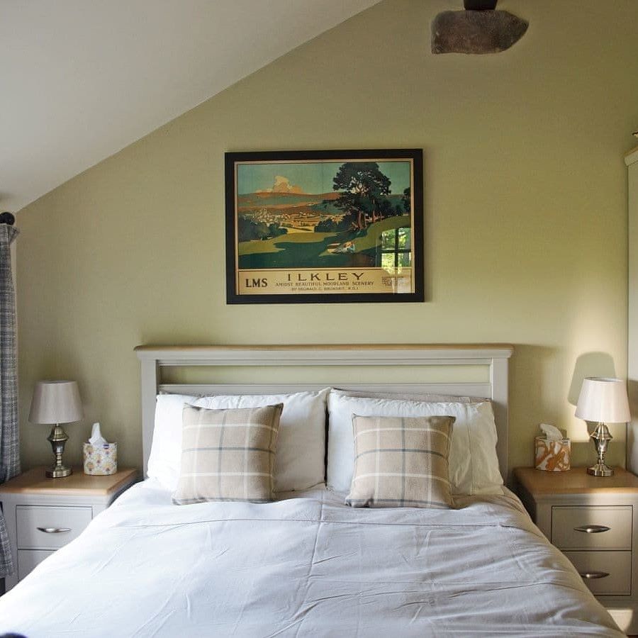 A double bed with a large retro poster for the town of Ilkley hangin on the wall above the headboard