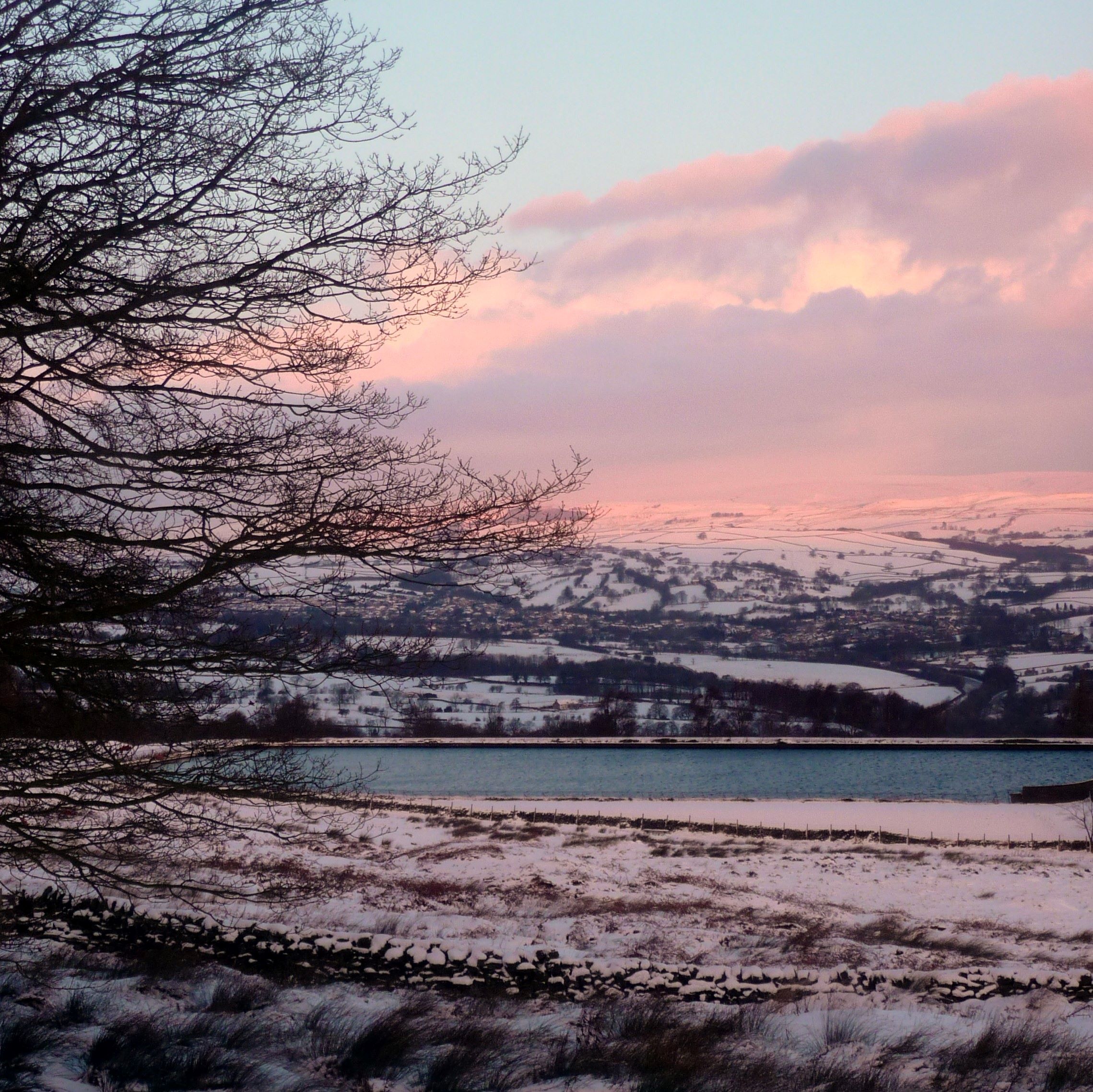 Countryside covered in snow with a reservoir in the middle distance